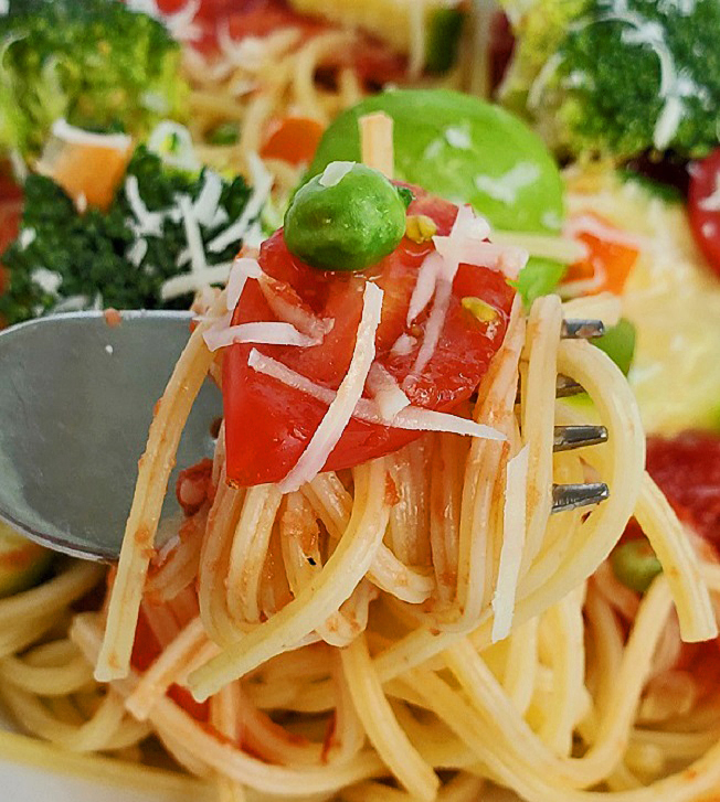 this is a close up photo of spaghetti and fresh vegetables on top with romano cheese grated on it