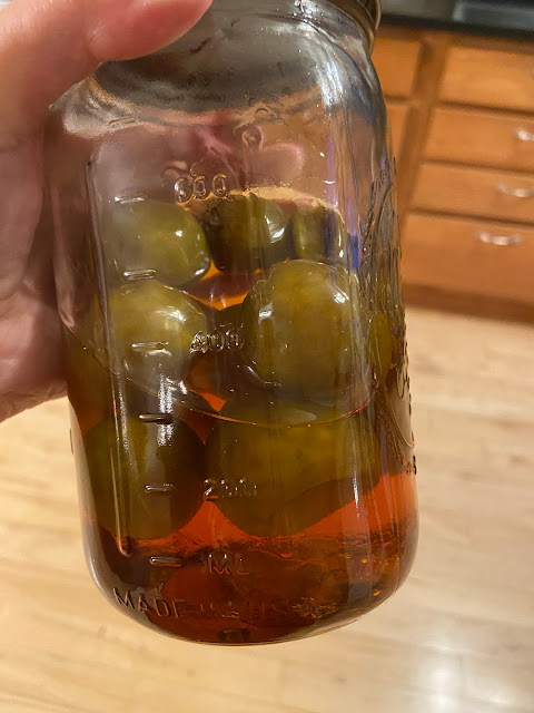 the author's hand holding a closed mason jar of yellow-brown limes floating in brown sugar syrup
