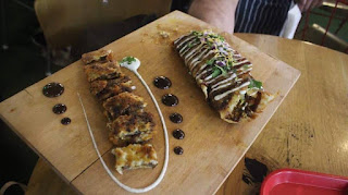 A selection of round light brown flatbreads with a thick white sauce drizzled all over on a large rectangular chopping board on a dark background.