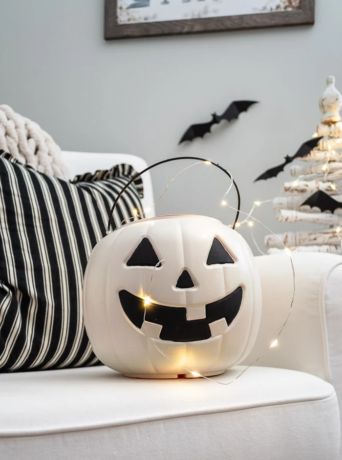 white painted jack o lantern candy bucket, fairy lights, striped pillow