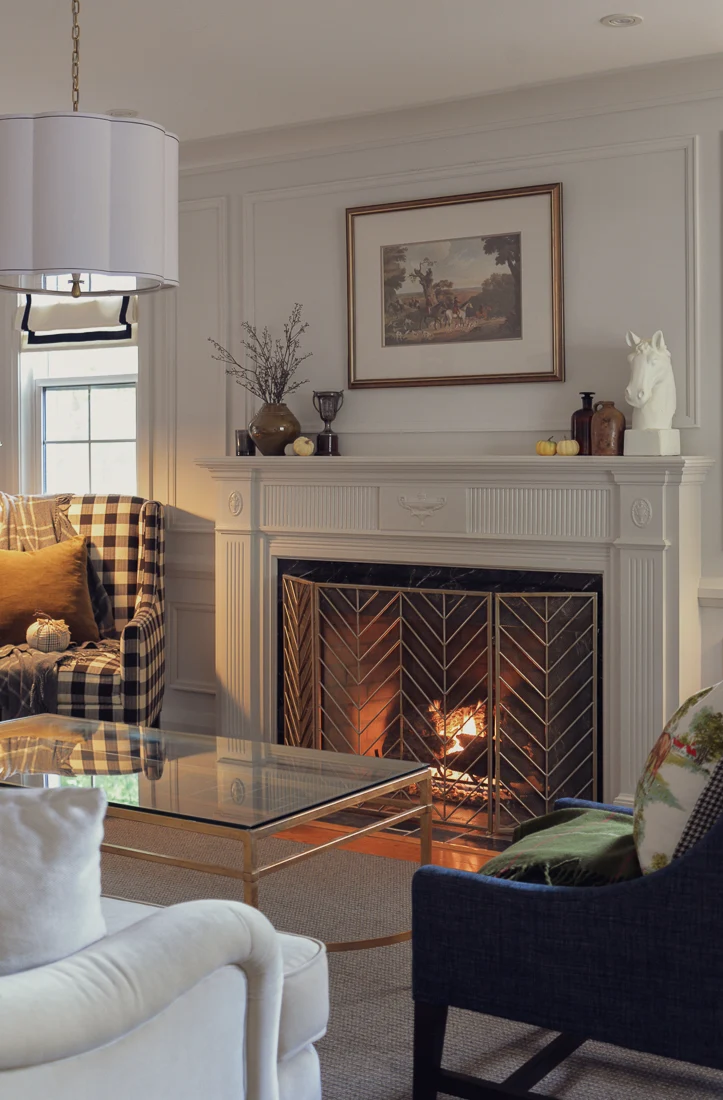 buffalo plaid armchair with throw pillows and plaid blanket beside a fireplace with traditional mantel and fall decor