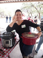 A woman in a black top holding a crock pot and leaning on another on a table.