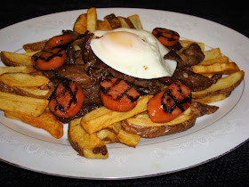 PORCIONES: 2 INGREDIENTES 250 g. posta negra, cortada en tiritas delgadas 1 longaniza cortada en rodajas o salchichón 2 huevos 4 papas grandes cortadas en palitos, reposando en agua fría 1 cebolla grande cortada en pluma 2 dientes de ajo 1 cucharadita de cilantro picado PREPARACIÓN Cortar la carne y las longanizas Yo las dejo con la piel las papas. Al cortar las papas en palitos déjelas en agua para que no se pongan negras. Ponga una olla grande con agua a hervir. Una vez que hierve el agua ponga las papas a cocinar por unos 5 minutos. Tienen que quedar duritas, no blandas. Sacar de la olla y poner en un colador y tirarles agua fría para que se enfríen. Dejar que escurra bien el agua. Terminar de secar con una toalla si se necesita. Freír las papas hasta que queden doraditas. Puede dejar las papas en el horno precalentado para que no se enfríen. Yo prefiero cocinar el salchichón en una grilla para marcarlos. Puede dejar en el horno para que no se enfríe. Poner aceite en una sartén y saltear la carne hasta que dore. Añadir la cebolla ajo y cilantro y saltear hasta que doren. Poner una sartén pequeñita a calentar y freír los huevos. Poner las papas fritas esparcidas en un plato y poner la carne cocinada con la cebolla en el centro con el huevo frito arriba y rodeada con el salchichón o longaniza.