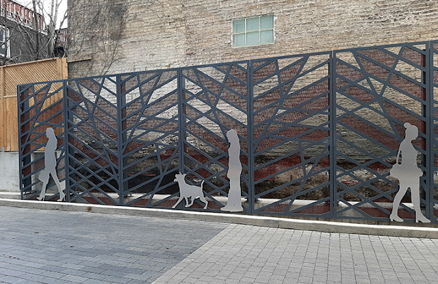 Large decorative metal screen with silhouettes of everyday figures attached to it, including a person walking a dog