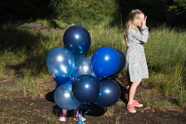 A small pair of feet poking out from a bunch of balloons next to a girl looking sideways and wiping her nose