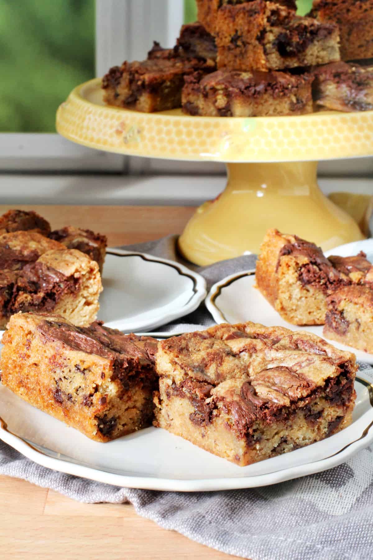 Chocolate Chip Marble Square Blondies on a yellow cake plate with a small plate in front.