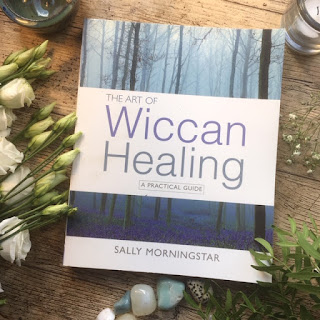 Copy of The Art of Wiccan Healing by Sally Morningstar laid next to some white flowers