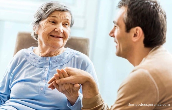 Hijo sosteniendo la mano de su madre anciana en una visita