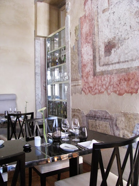 cadeiras e mesas com talheres e pratos ao lado de uma parede com  pintura do séc.. XVIII