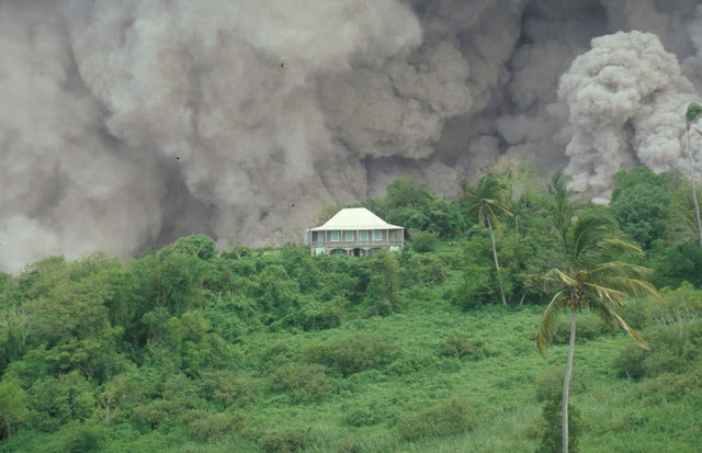 The Tar River Estate House on 17th September 1996 with a dome-collapse pyroclastic flow passing behind down the Tar River valley. This dome collapse continued for more than nine hours. A large part of the dome collapsed on 17th September and this caused a rapid reduction in pressure over the vent at the summit of the volcano. As a result, shortly before midnight, there was a magmatic explosion during which blocks of lava 1.5 m. in diameter were blasted 2.1 km. from the dome. The ongoing eruption of the Soufriere Hills Volcano has devastated much of the small Caribbean island of Montserrat. The eruption of the lava dome-building volcano began in 1995 and volcanic hazards have included pyroclastic flows, pyroclastic surges, vulcanian explosions, lateral blasts, ash clouds and lahars.