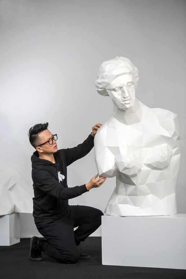 crouching young man next to all-white low poly paper sculpture male bust