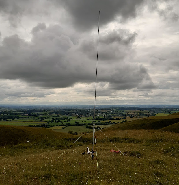 The aerial in use on a hilltop. It is mounted on a short wooden post and supported with three guy ropes.