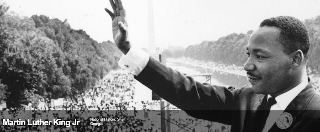 Image from the website for the Martin Luther King Jr. National Historic Site. Image shows Dr. King standing with an upraised arm at the National Mall with the Washington Monument in the background.