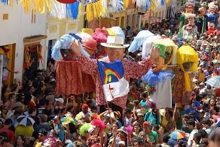  desfile de carnaval com bonecos gigantes nas ruas e uma mltidão de pessoas seguindo 