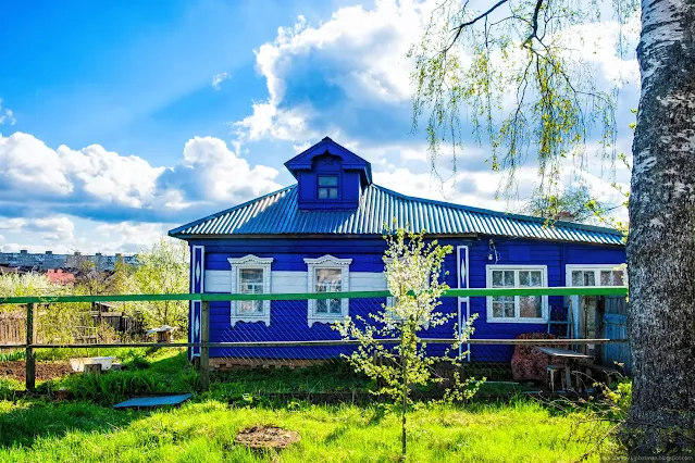 Деревенский дом с резьбой на фоне многожтажек