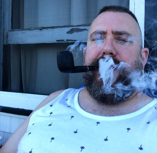 Sitting on a porch bearded bear smoke all around face wearing a white wife beater