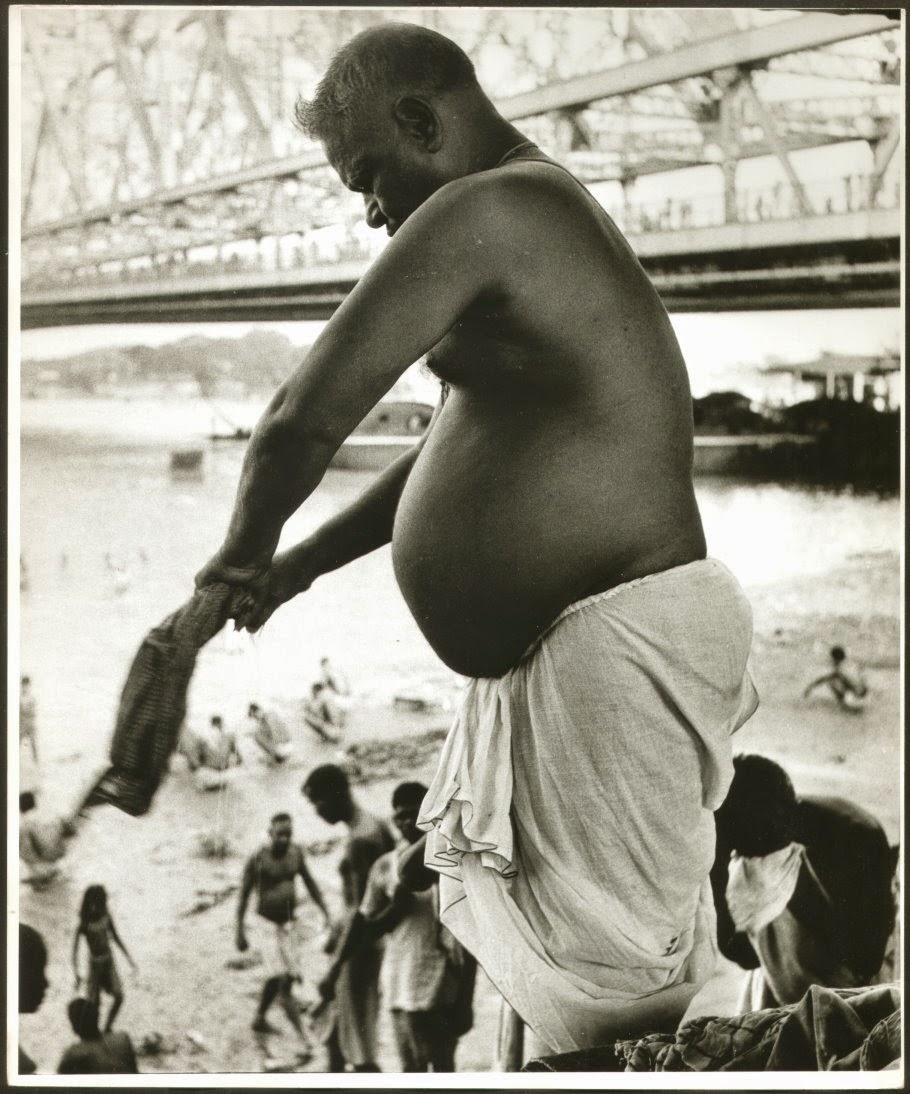 A Man is Wringing Out his Towel after bath in River Ganges (Ganga) in Kolkata (Calcutta). Howrah Bridge (Rabindra Setu) is visible in background - c1980's
