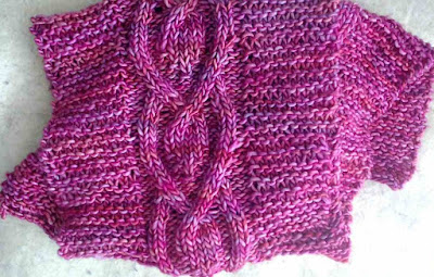 A pink scarf worked in bulky-weight yarn. The scarf is knit in garter stitch with a centre cable motif