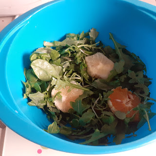 A large, plastic, blue bowl photographed from above. In the bowl are green leaves, and slices of grapefruit and orange.