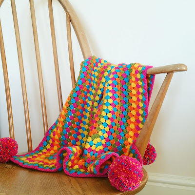 A colourful giant granny square blanket draped over a chair.