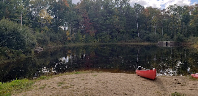 Red canoe on shore in front of small pond.