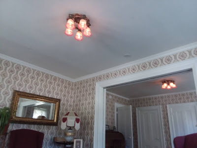 The double parlor with Victorian wallpaper and two new antique-styled chandeliers, each with five pink etched domes, visible