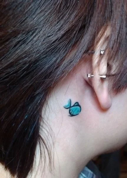 Chica mostrando su cuello con un tatuaje de un pez  azul agua