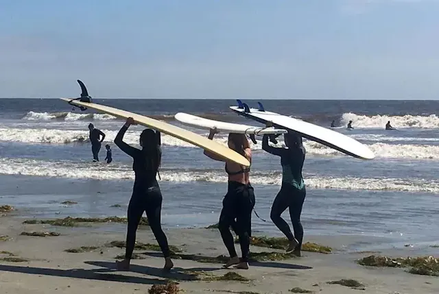 Three women taking surfer board on their heads