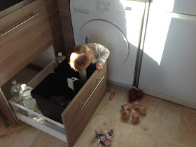 Toddler bent over in kitchen drawer, onions scattered across the foor