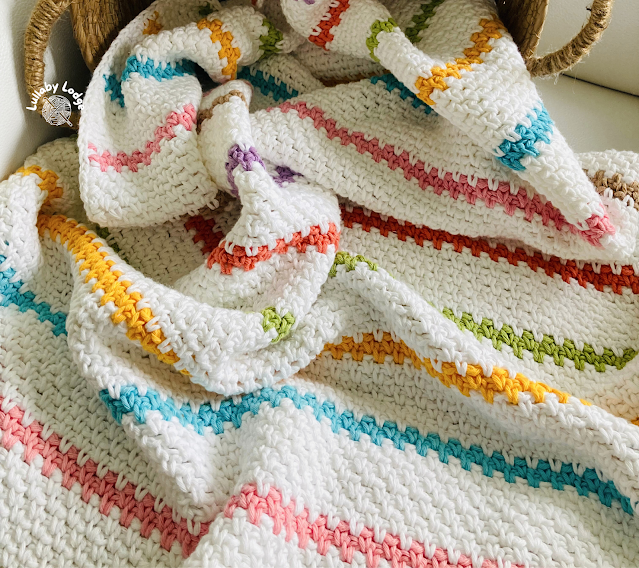 White crochet baby blanket with pink, blue, yellow, green, and soft brown stripes.