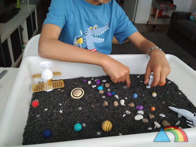 Niño jugando con bandeja sensorial del espacio (arroz teñido de negro, miniaturas de planetas del Sistema Solar, piedras de colores, naves y astronautas de juguete)