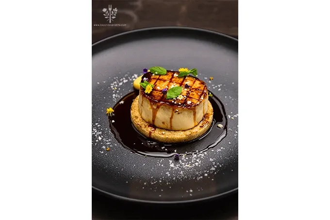 Seared Foie Gras with Balsamic Glaze plated with fig compote, micro basil, and edible flowers on a black ceramic plate.