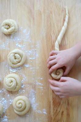 Schnecken aus Hefeteig werden von Kinderhänden auf einem bemehlten Holzbrett geformt.