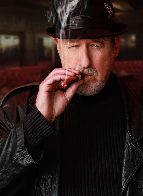 7/12 Middle-aged man who looks like Robert Englund wearing black leather jacket hat smoking a study