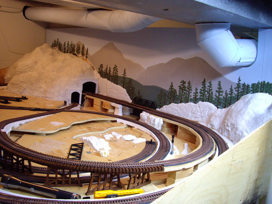 A foamboard backdrop painted with trees, mountains, and a blue sky installed on a model railroad layout
