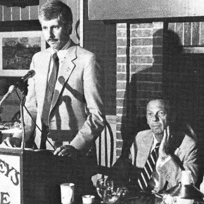 GM Poile speaks at a press event, while Pollin wonders what happened to his vodka tonic.