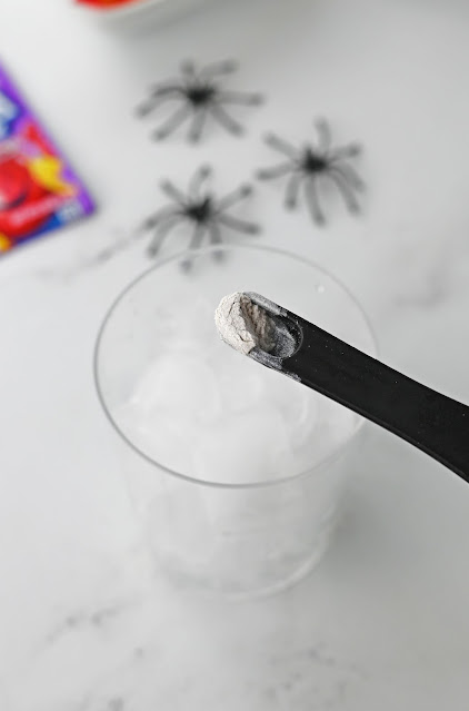 edible shimmer powder on a measuring spoon over a glass.