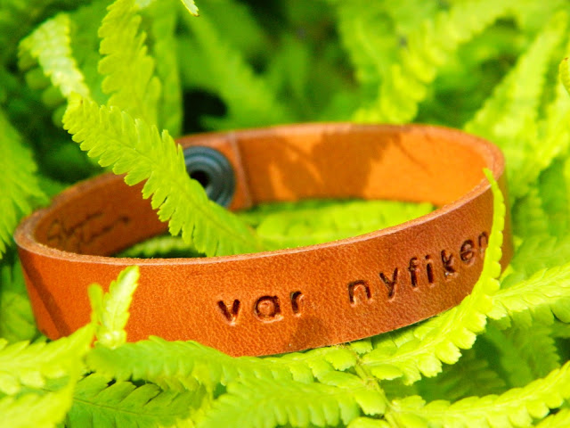 A brown leather bracelet made by Stina Glaas sitting on a green fern