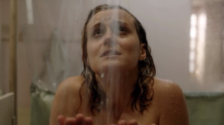 Piper Chapman olhando para o alto com cara de sofrimento pelada tomando banho na prisão, a imagem só mostra do ombro nu pra cima.