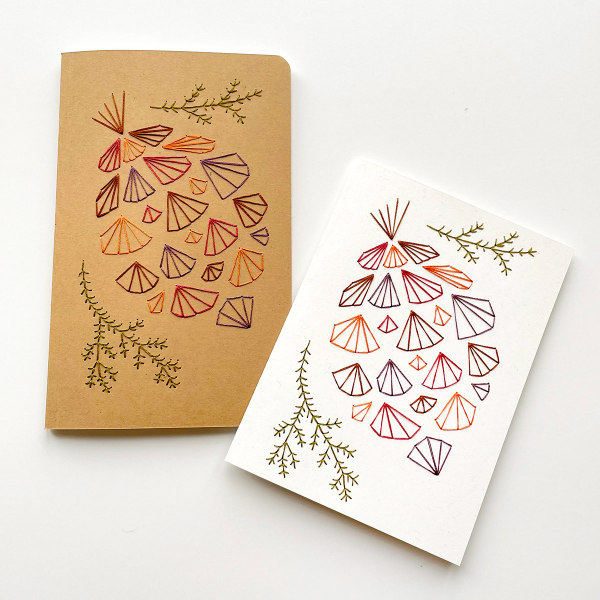 geometric pinecone paper embroidery on two notebook covers, one white, one kraft paper