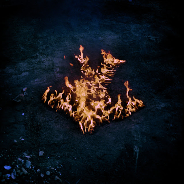 A imagem apresenta um gramado verde e uma silhueta humana pegando fogo no centro da foto.
