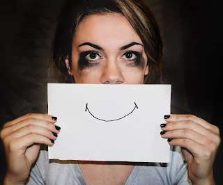 A young female with heavy bruising to the eyes and a false smile drawn on a paper to hide her own mouth!