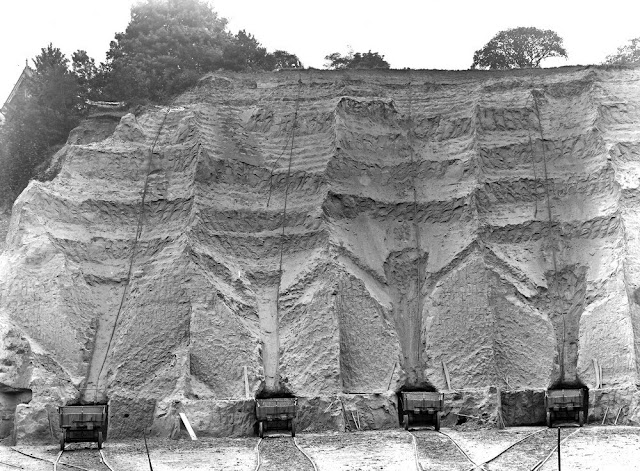 Parish's Loam Work, Erith. Looking S. This is (really) the southern portion of the great pit, entered along the southern tramline. View looking south and shows mode of working. A small adit is made at foot of the face. The overlying sand is shovelled down, with the truck placed at mouth of adit. This causes the curious aspect of the face. The sand does not show bedding unless seen very closely. This exposes the whole thickness of the Thanet Sand, about 70 feet, with an ill-defined capping of the pebbly series.