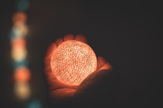 Against a dark background, a hand reaches out away from the viewer, holding a glowing ball. The hand is barely illuminated, aside from the light from the ball.