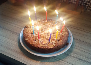 A photo of a cake on a wooden counter with 10 birthday candles alight on it in a circle around the edge.