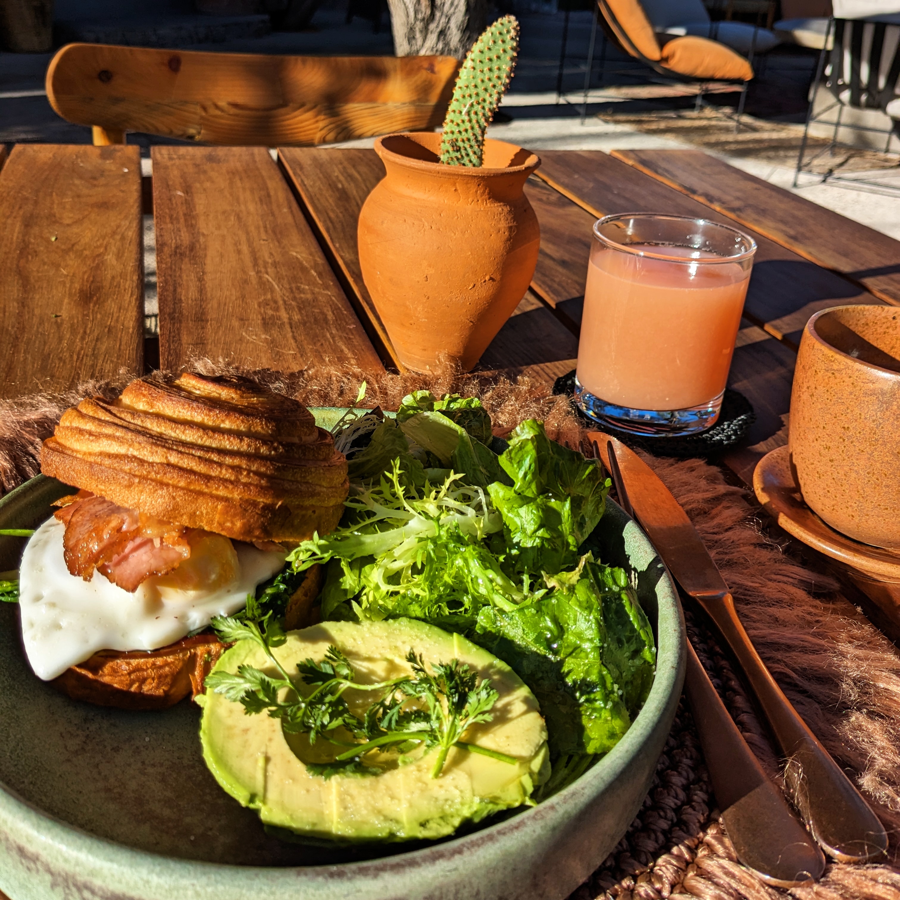 A pastry sandwich with avocado and juice on a table in the sun for breakfast at Our Habitas hotel in San Miguel de Allende, Mexico