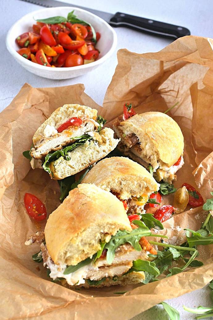 Recipe for a sandwich with a breaded veal cutlet, arugula, tomato salad and burrata cheese, drizzled with balsamic vinegar.