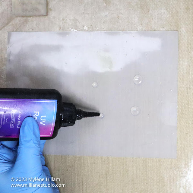 Gloved hand squeezing dots of clear UV resin onto a silicone mat.
