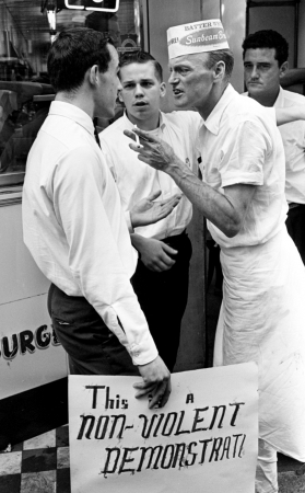 “Archie Allen, left, a member of the civil rights demonstrators, talks with employees of the Tic Toc Restaurant on downtown Church Street April 27, 1964. Moments later, Allen was attacked by the employees and knocked down on the sidewalk.” 