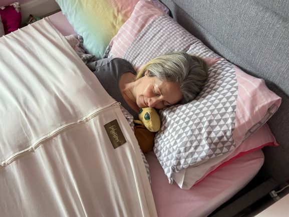 middle aged woman lying in a bed covered by duvet and fidgetbum zipped sheet, pretending to sleep